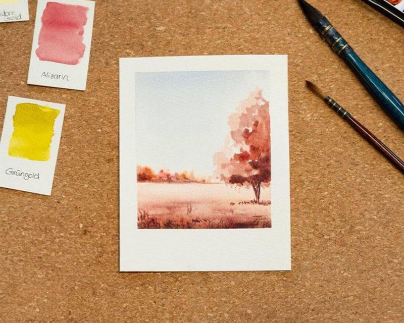 Eine rötlich, gemalte Herbstlandschaft auf Aquarellpapier, daneben ein Pinsel und Farbkarten, Bild verlinkt zum Workshop.