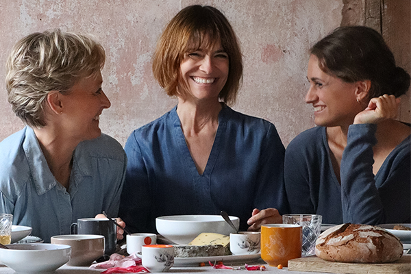 Drei Frauen sitzen lachend an einem gedeckten Tisch und lachen
