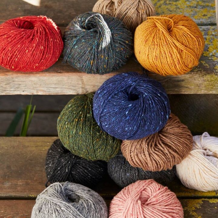 Mehrere bunte Wollkn&auml;uel auf h&ouml;lzernen Stufen verteilt. Farben umfassen Rot, Blau, Gelb, Gr&uuml;n, Braun, Grau und Schwarz, einige mit bunten Sprenkeln.
