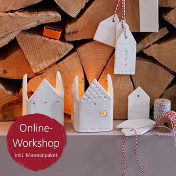 Zwei weiße, hausförmige Kerzenhalter aus Keramik mit eingeschnittenen Mustern stehen vor gestapeltem Kaminholz. Daneben sind weiße Anhänger, Garnrollen und ein Hinweis auf einen "Online-Workshop inkl. Materialpaket" zu sehen.