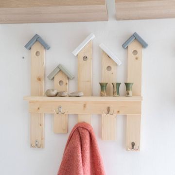 Holz-Hängeregal in Form von Häusern mit drei Haken unten, zwei kleinen Vasen und drei Steinen oben, an einer weißen Wand montiert. Ein orangefarbenes Tuch hängt an einem der Haken.