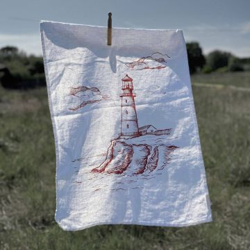 Weißes Geschirrtuch mit roter Zeichnung eines Leuchtturms auf Klippen, aufgehängt an einer Wäscheklammer im Freien. Hintergrund zeigt eine Landschaft bei blauem Himmel.