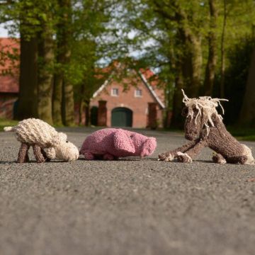 Drei gestrickte Stofftiere liegen auf einer hellblauen Decke: ein rosa Schwein oben links, ein weißes Schaf mit rosa Blume im Maul oben rechts und ein braunes Pferd mit heller Mähne und Schweif unten im Vordergrund. Alle Tiere bestehen aus Wolle und haben