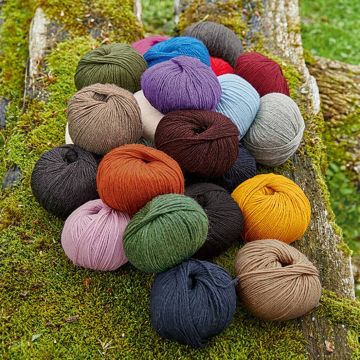 Mehrere bunte Wollknäuel in verschiedenen Farben wie Orange, Grün, Blau und Lila liegen auf moosbedeckten Baumstämmen.