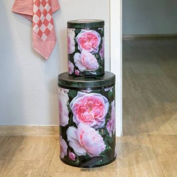 Zwei runde Mülleimer in unterschiedlicher Größe mit rosafarbenem Blumenmuster auf dunklem Hintergrund stehen übereinander auf einem hellen Boden vor einer weißen Wand; links hängt ein rot-weiß kariertes Geschirrtuch.