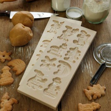 Zwei Holzmodelle mit Ausstanzungen für Lebkuchenfiguren wie Schneemann, Tannenbaum und Lebkuchenmännchen, umgeben von Teigkugeln, fertigen Lebkuchen und Backzutaten auf einer Holzarbeitsfläche.