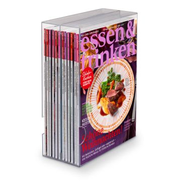 Ein transparentes Zeitschriftenregal mit mehreren Ausgaben der Zeitschrift "essen & trinken", die vorne sichtbar ist. Das Cover zeigt ein Festtagsgericht auf einem Teller und trägt den Titel "Schöne Weihnachten!".