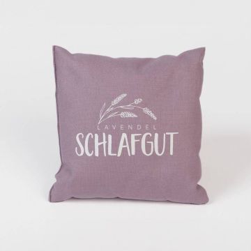 Fliederfarbenes Kissen mit der Aufschrift „Lavendel Schlafgut“ und einer stilisierten Lavendelzeichnung in Weiß, vor weißem Hintergrund.