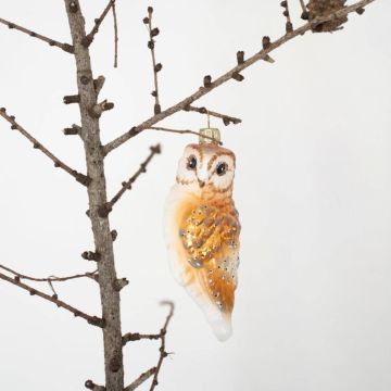Glasschmuck in Form einer Eule hängt an einem kahlen Ast vor einem weißen Hintergrund, verziert mit goldenen und weißen Details und einem goldenen Aufhänger.