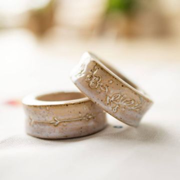 Zwei beige Keramikserviettenringe mit eingeprägtem floralen Muster liegen aufeinander auf einem hellen Untergrund. Die Oberfläche ist leicht gesprenkelt, die Muster zeigen Blumen und einen Pfeil.
ChatGPT fragen