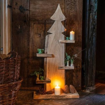 Holzdekor im Tannenbaum-Design mit integrierten Ablagen, auf denen Kerzen und Pflanzen arrangiert sind. Der Boden ist mit Tannenzapfen und einer brennenden Kerze dekoriert. Es lehnt gegen eine rustikale Holzwand in gemütlichem Ambiente.