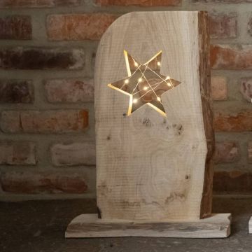 Ein Holzbrett mit Sternenausschnitt, hinter dem Lichterketten leuchten, steht vor einer Ziegelwand auf einem dunklen Untergrund.