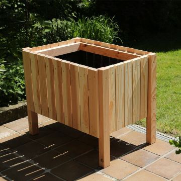 Holzhochbeet auf einer Terrassenfliese, umgeben von Grünpflanzen. Das rechteckige Beet ist aus senkrechten Holzlatten gefertigt und steht auf vier Beinen. Es ist leer und bereit zum Bepflanzen.