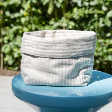 Gefaltet offener hellgrauer gestreifter Stoffkorb auf einem blauen Tisch, draußen platziert. Unscharfer grüner Laub-Hintergrund.