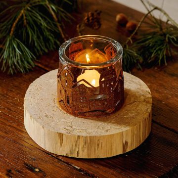 Kerzenglas mit eingeschnittener Stadtsilhouette aus Metall, darin eine brennende Kerze. Der Halter steht auf einer runden Holzplatte, umgeben von Tannenzweigen und Nüssen auf einem Holztisch.