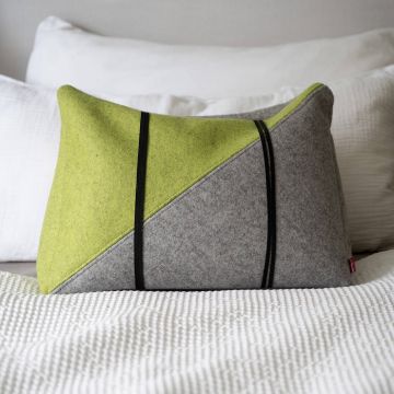 Rechteckiges, zweifarbiges Kissen aus grauem und grünem Stoff mit schwarzen Streifen, dekorativ auf einem weißen Bett drapiert.