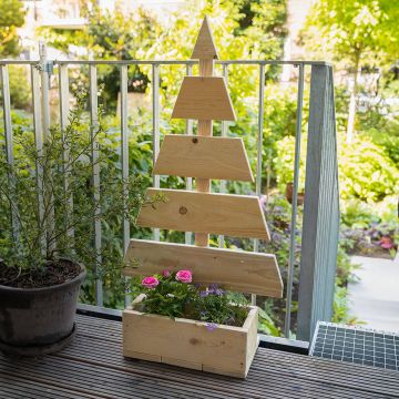 Ein stilisierter Holzweihnachtsbaum mit Lichterkette steht an einer Wand. Unten im Holzkasten befinden sich Tannenzweige und eine leuchtende Stern-Dekoration. Der Boden besteht aus hellen Holzdielen und Fliesen.
