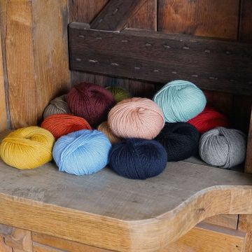 Zwölf Garnknäuel in verschiedenen Farben, darunter Gelb, Blau, Schwarz, Rosa und Grau, liegen in einer hölzernen Ecke.
