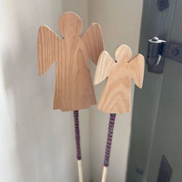 Zwei Holzengel-Dekorationen auf Stäben, die mit bunter Wolle umwickelt sind. Der größere Engel ist links, der kleinere rechts. Sie lehnen an einer Wand neben einer grün gestrichenen Tür.