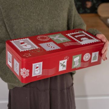Eine Person hält eine rechteckige rote Blechdose mit weihnachtlichen Briefmarkenmotiven, darunter Schneemänner, Elche und Schneeflocken. Die Dose hat einen dekorativen Charakter und könnte für Geschenke oder Lagerung verwendet werden.