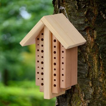 Helles Insektenhotel aus Holz mit glatten Oberflächen, rechteckigen Formen und vielen kleinen runden Löchern, vor grünem Hintergrund.