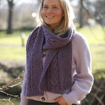 Junge Frau mit langem, lila Wollschal und passendem Pullover, grobe Strickstruktur, draußen im hellen Tageslicht.