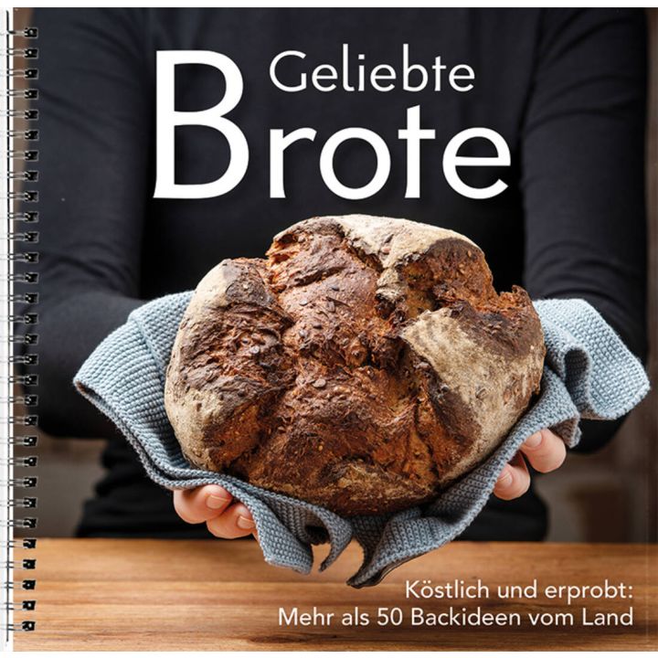 Eine Person hält ein rundes, gebackenes Brot in einem Handtuch. Auf dem Cover steht "Geliebte Brote", darunter "Köstlich und erprobt: Mehr als 50 Backideen vom Land". Spiralbindung erkennbar.