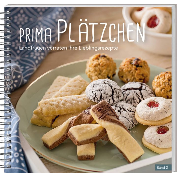Ein spiralgebundenes Backbuch mit dem Titel „Prima Plätzchen – Landfrauen verraten ihre Lieblingsrezepte, Band 2“. Auf dem Cover sind verschiedene Plätzchen auf einem Teller arrangiert, darunter Schokocookies, Kokosmakronen und Buttergebäck.