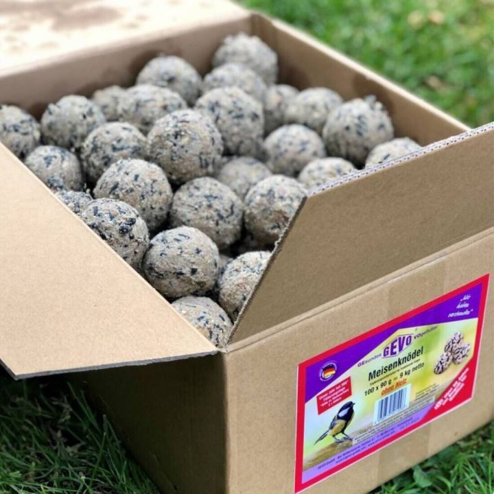 Karton auf Gras mit vielen runden Meisenknödeln. Auf dem Karton befindet sich ein Etikett mit Produktinformationen.