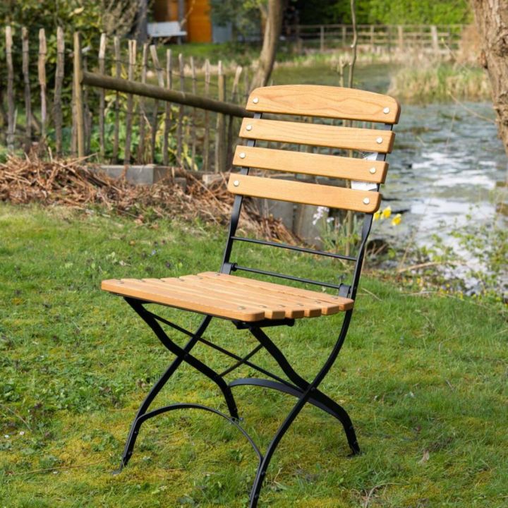 Gartenstuhl mit Sitzfl&auml;che und R&uuml;ckenlehne aus Robinienholz, mit Gestell aus pulverbeschichtetem Stahl, steht aufgeklappt auf einer Wiese.