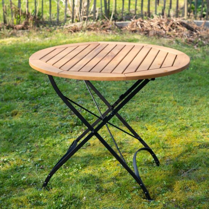 Runder Gartentisch mit hölzerner Tischplatte und schwarzen Metallbeinen, stehend auf einer grünen Rasenfläche.