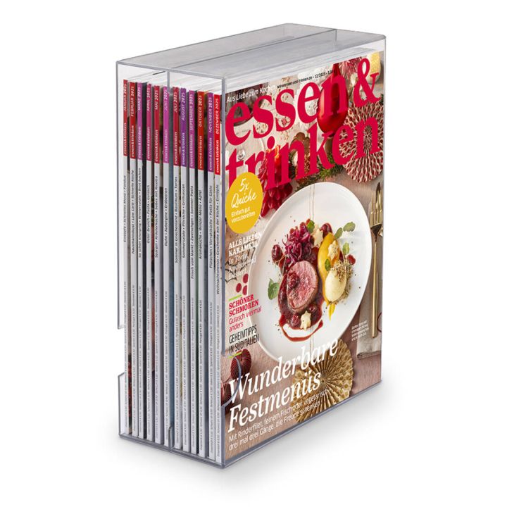 Ein transparentes Zeitschriftenregal mit mehreren Ausgaben der Zeitschrift "essen & trinken", die vorne sichtbar ist. Das Cover zeigt ein Festtagsgericht auf einem Teller und trägt den Titel "Schöne Weihnachten!".