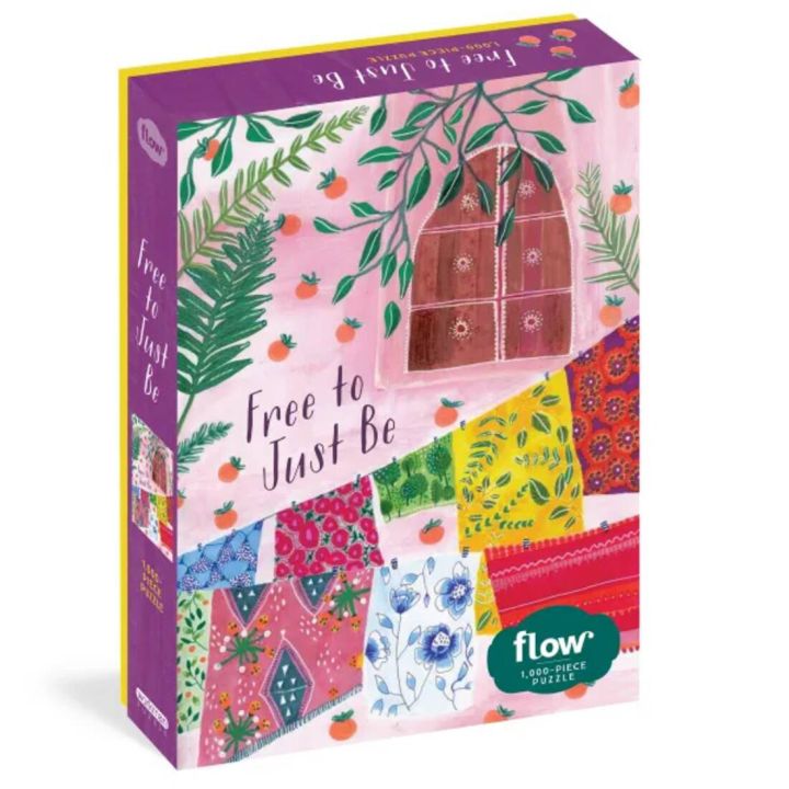 Puzzle-Schachtel mit dem Titel &bdquo;Free to Just Be&ldquo;, zeigt bunte Stoffmuster, ein Fenster mit Pflanzen und das Logo &bdquo;flow 1.000-PIECE PUZZLE&ldquo; auf der Vorderseite.