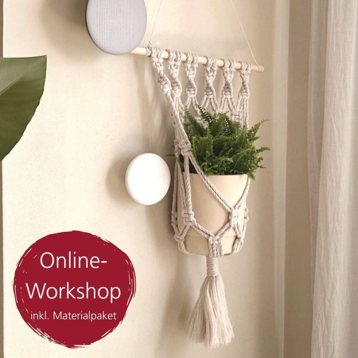 Makramee-Blumenampel mit Topf und Pflanze hängt an Wandhaken; Text im roten Kreis: „Online-Workshop inkl. Materialpaket“; neutrale Wand, dekorative Nutzung.