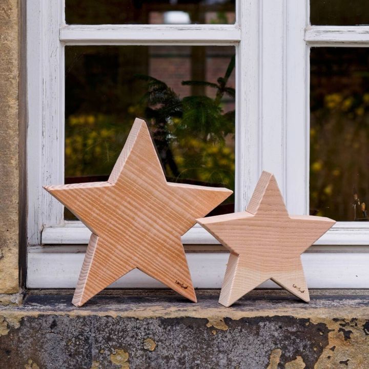 Zwei hölzerne Sterne, einer größer, einer kleiner, stehen auf einer Fensterbank vor einem Fenster mit weißen Rahmen.