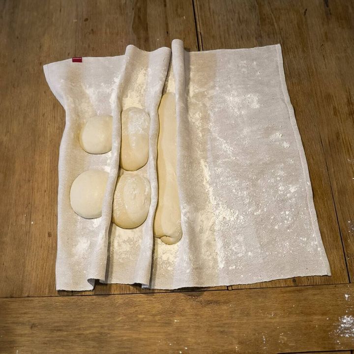Vier Teiglinge liegen auf einem bemehlten Leinentuch mit Falten zur Trennung; das Tuch befindet sich auf einer Holzoberfläche.