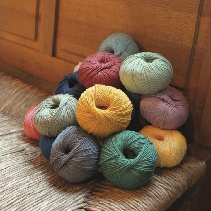 Mehrfarbige Wollknäuel in verschiedenen Farben, darunter Gelb, Blau, Rot und Grün, liegen gestapelt auf einem geflochtenen Sitz. Sie sind rundlich geformt und zeigen eine weiche Textur, geeignet zum Stricken oder Häkeln.