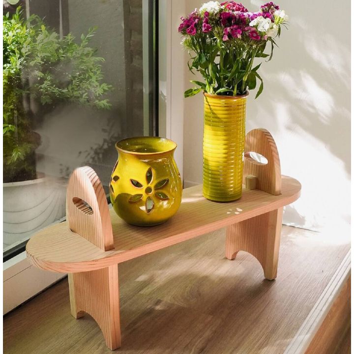 Kleiner Holzhocker steht am Fenster, darauf gelbe Keramikvase mit Blumen und gelbes Windlicht.