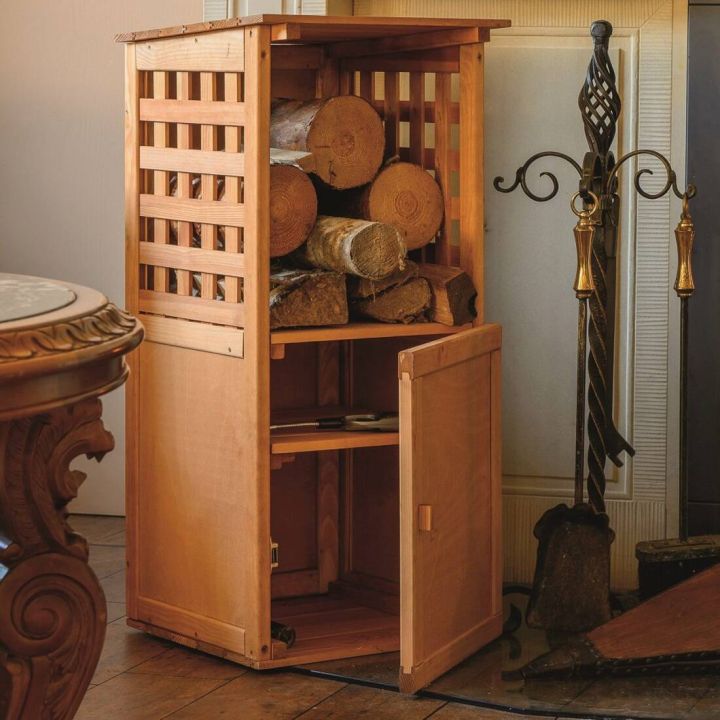 Holzregal aus hellem Holz mit Gitterdesign, offenem und geschlossenem Fach. Oben lagern geschnittene Holzscheite, das untere Fach mit ge&ouml;ffneter T&uuml;r zeigt leeren Stauraum. Rechts stehen Kaminbestecke mit verzierten Griffen.
