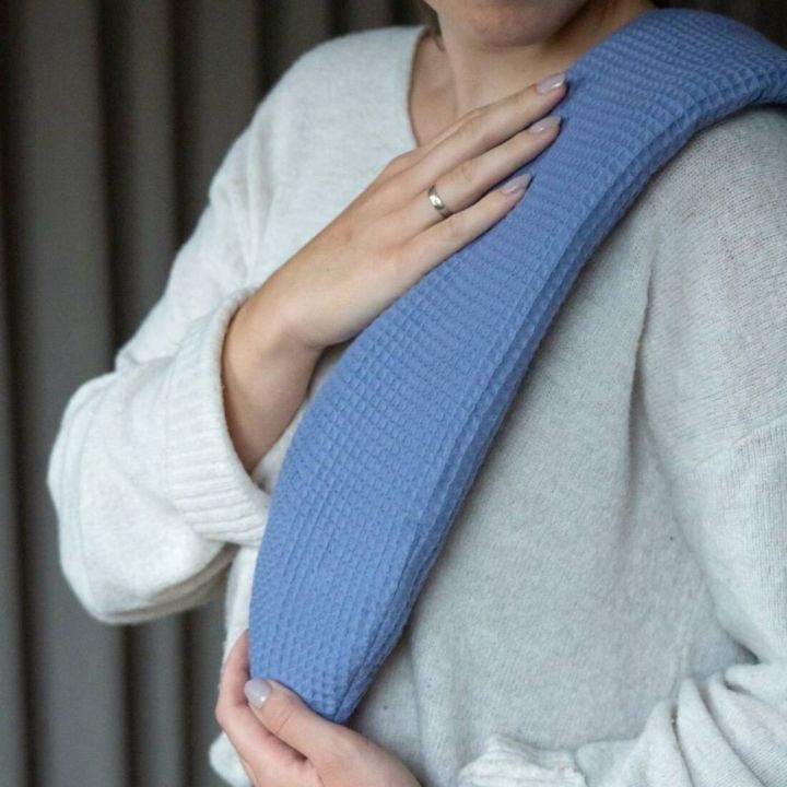 Person in wei&szlig;em Pullover h&auml;lt ein blaues, gewelltes Kissen oder Produkt &uuml;ber der Schulter und auf der Brust. Man sieht keine Gesichter, nur H&auml;nde und Oberk&ouml;rper. Klarer Fokus auf dem Produkt.