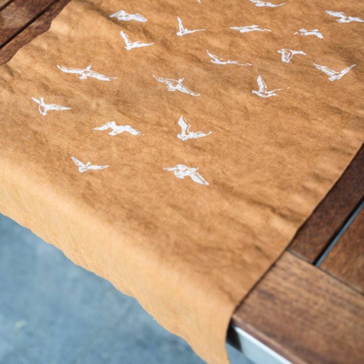 Brauner Stoffläufer auf Holztisch, verziert mit weißen Vogelmotiven, von oben fotografiert.