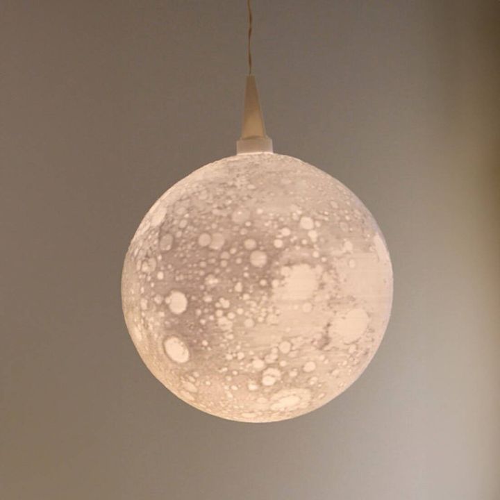 Runde, h&auml;ngende Deckenleuchte in Form des Mondes mit kraterartiger, strukturierter Oberfl&auml;che. Die Leuchte strahlt sanftes Licht und ist &uuml;ber ein Kabel befestigt.