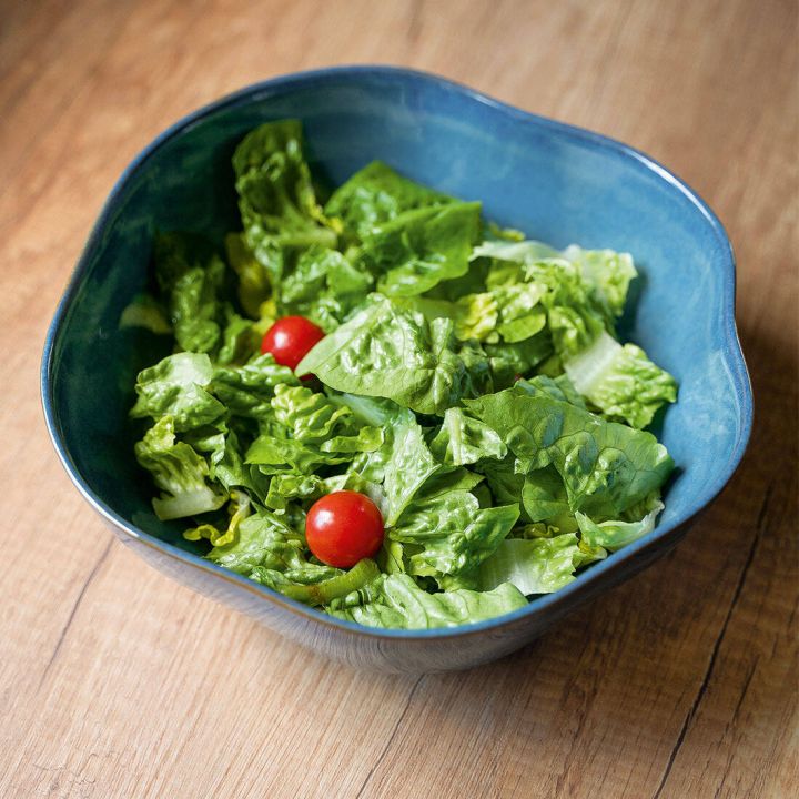 Blauer Sch&uuml;ssel mit gr&uuml;nem Blattsalat und zwei roten Cherrytomaten auf hellem Holzuntergrund, fotografiert von schr&auml;g oben.