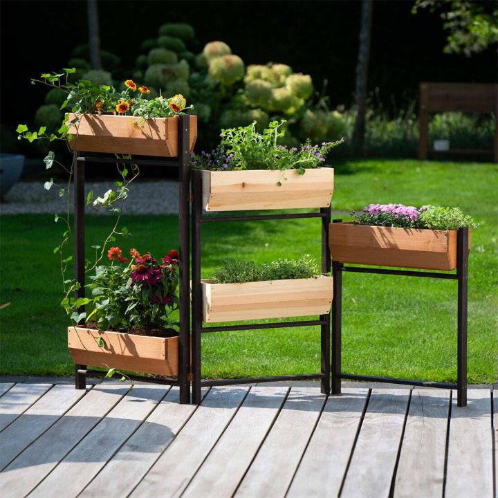 Metallrahmen mit mehreren h&ouml;lzernen Pflanzk&auml;sten auf Terrasse, bepflanzt mit bunten Blumen und gr&uuml;nen Kr&auml;utern, vor gr&uuml;nem Rasen im Garten.