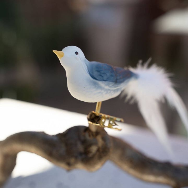 Dekorative M&ouml;we mit blau-wei&szlig;em Federkleid und Federk&ouml;rper auf einem Ast platziert, befestigt mit einer goldenen Klammer. Verschwommener Hintergrund.