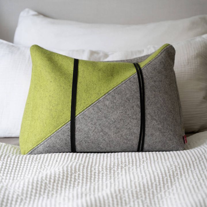 Rechteckiges, zweifarbiges Kissen aus grauem und gr&uuml;nem Stoff mit schwarzen Streifen, dekorativ auf einem wei&szlig;en Bett drapiert.