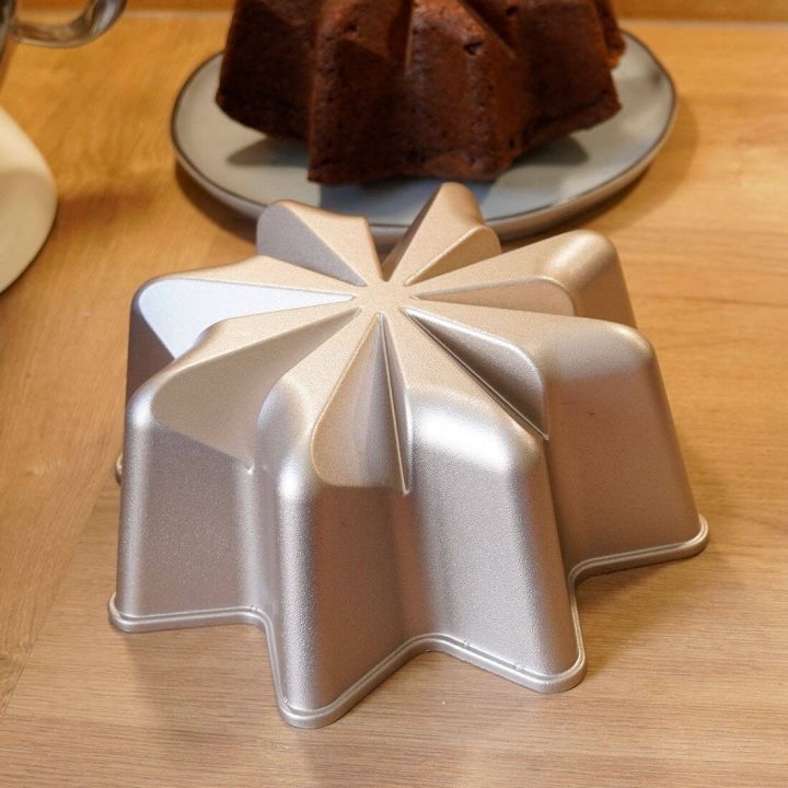Silberfarbene Backform in Sternform auf Holztisch, neben einem gebackenen Schokoladenkuchen auf Teller. Die Form ist metallisch und dient zur Herstellung von sternförmigen Kuchen.