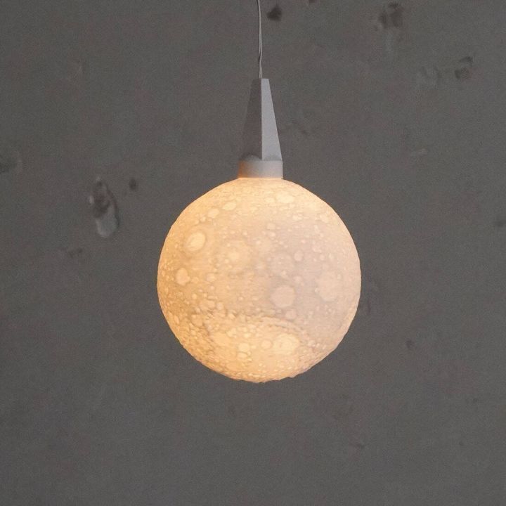 Leuchtkugel mit matter, strukturierter Oberfläche, aufgehängt an einem Kabel. Die Oberfläche ist leicht unregelmäßig und ähnelt einer Mondlandschaft. Die stimmungsvolle Beleuchtung erzeugt sanftes Licht.