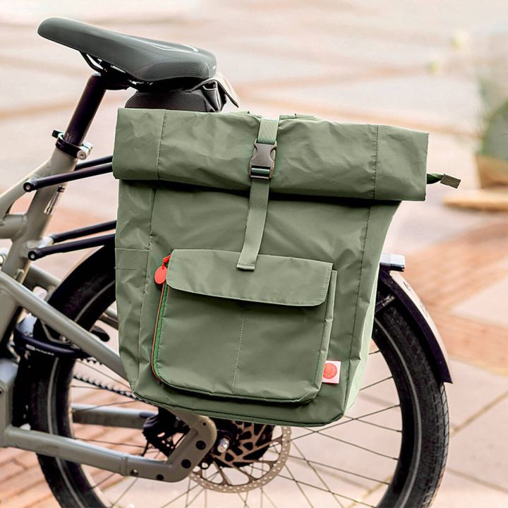 Grüne, wasserdichte Fahrradtasche mit Rolltop-Verschluss und großer Fronttasche, seitlich am Gepäckträger eines Fahrrads befestigt; Fokus auf Befestigung am Rad und Stauraum der Packtasche.