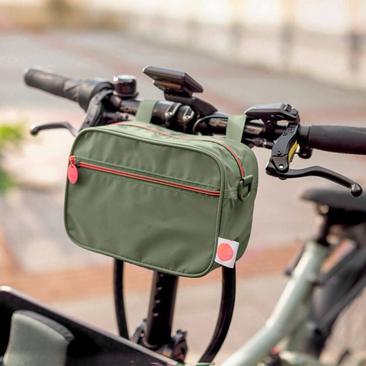 Grüne, rechteckige Lenkertasche mit Reißverschlussfach und Kontrastzippern, mittels Schlaufen zentral am Fahrradlenker befestigt; Fokus auf Stauraum für Kleinteile und die Positionierung der Tasche im Sicht- und Griffbereich beim Fahren.